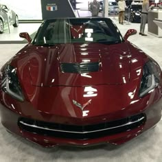 the front end of a red sports car on display at an auto show with people in the background