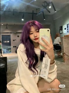 a girl with purple hair is holding up her cell phone