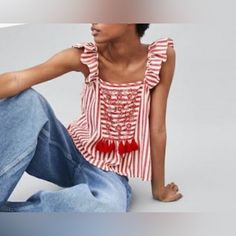 a woman is sitting on the ground wearing jeans and a striped top with red accents