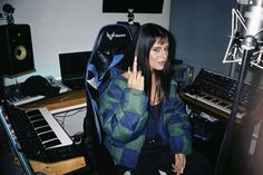 a woman sitting in front of a keyboard and sound equipment with her hand up to the side