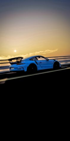 a blue sports car driving down the road at sunset with a surfboard on top of it