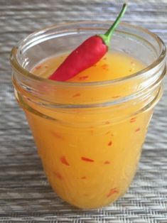 a glass jar filled with orange liquid and a red pepper on top