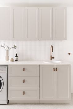 a washer and dryer in a white kitchen with cabinets on either side of the sink