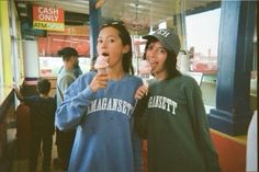 two young women eating donuts in front of a store window at an ice cream shop