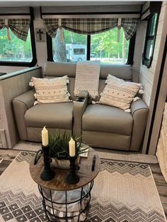 a living room area with couches, table and windows in the back side of an rv