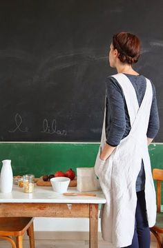 a woman standing in front of a blackboard with food on the table next to her