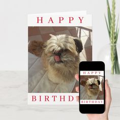 a person holding up a cell phone with a happy birthday card on it and a dog in the background