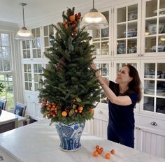 a woman is decorating a christmas tree with oranges in a blue and white vase