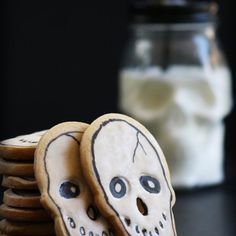 cookies decorated to look like skulls are stacked on top of each other with a jar of milk in the background