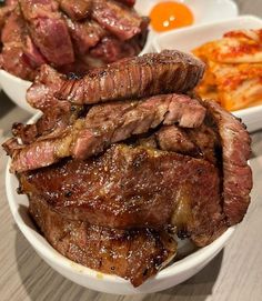 some meat is sitting in a white bowl on a table next to other food items