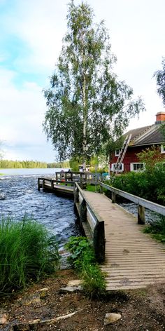 a wooden bridge over a body of water next to a red house with trees in the background