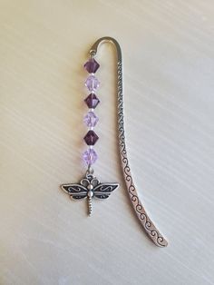 a metal hook with a dragon charm attached to it on a white table top next to a string of beads