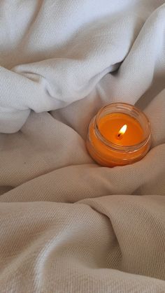 an orange candle sitting on top of a white bed sheet next to a light brown blanket