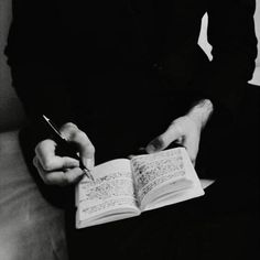 a person sitting on a couch with an open book and pen in their hand while writing