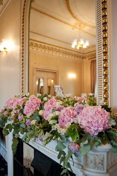 pink flowers are in a window box on the mantle