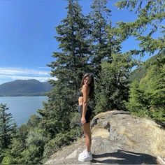 a woman standing on top of a large rock next to trees and the ocean in the background