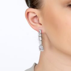 Step into a world of glamour with the Crawford Drop Earrings in Silver White. Exquisitely fashioned  and resplendent with dazzling simulated diamonds, these earrings exude an Art Deco charm that’s both vintage and timeless.  The elegant drop design features five rectangular settings. Each setting is graced with a unique arrangement of gemstones, crowned by a single radiant simulated diamond at the bottom, encircled by a stunning array of baguette-cut stones.   These earrings are designed for bot Luxury Baguette Diamond Earrings For Formal Events, Elegant Formal Earrings With Baguette Diamonds, White Gold Baguette Diamond Earrings For Evening, Luxury Silver Baguette Cut Diamond Earrings, Luxury Bridal Earrings With Baguette Diamonds For Anniversary, Dazzling Baguette Diamond Earrings For Formal Events, Dazzling Baguette Diamond Formal Earrings, Dazzling Baguette Diamond Earrings For Formal Occasions, Luxury Brilliant Cut Diamond Earrings For Evening