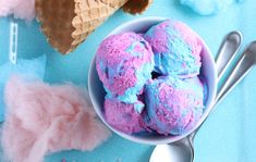 three scoops of blue and pink ice cream in a bowl next to two spoons