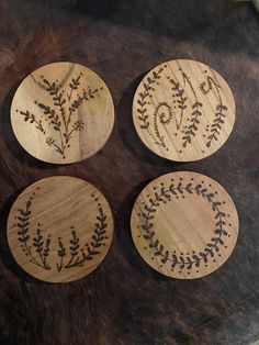 four wooden coasters with designs on them sitting on a fur covered table top,