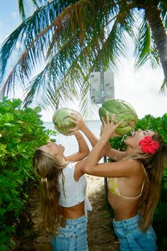 two girls are holding up watermelons in front of their faces while standing under a palm tree