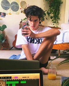 a young man sitting on the floor looking at his cell phone and drinking orange juice