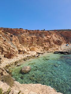 people are standing on the edge of a rocky cliff by the water's edge