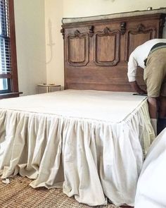 a man working on a bed in a room with a wooden headboard and white bedspread