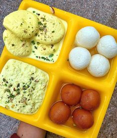 a person's hand holding a yellow tray filled with different types of food items