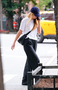 a woman is walking down the street talking on her cell phone while wearing black pants and a white t - shirt