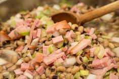 a mixture of beans, ham and onions in a pan with a wooden spoon on the side