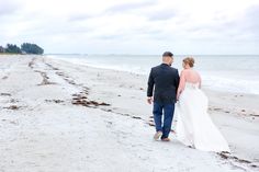 a bride and groom walking on the beach