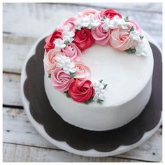 a white cake with pink and red flowers on top, sitting on a wooden table