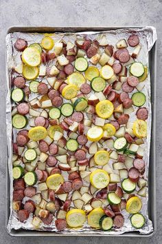 a pan filled with sausage, potatoes and zucchini on top of aluminum foil