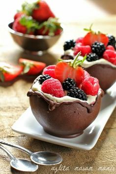 chocolate dessert with berries and whipped cream on a white plate next to silver spoons