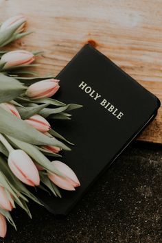 a bible with pink tulips on top of it next to a bunch of flowers