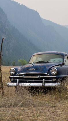 an old car is parked in the middle of a field with mountains in the background