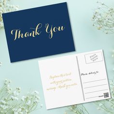 a blue and gold thank you card next to some white flowers on a green background