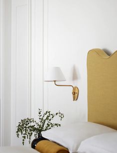 a bed with white sheets and pillows next to a wall mounted lamp on the wall