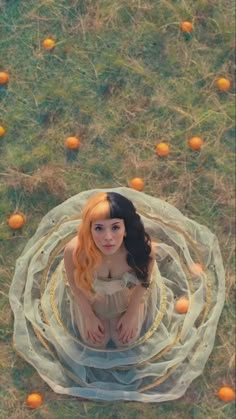 a woman with long hair sitting on the ground surrounded by oranges and mesh netting