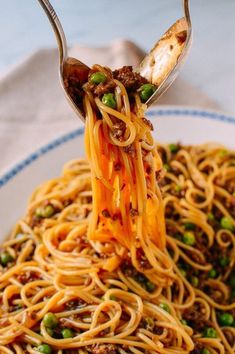 a fork full of spaghetti with peas and meat on it is being lifted from the plate