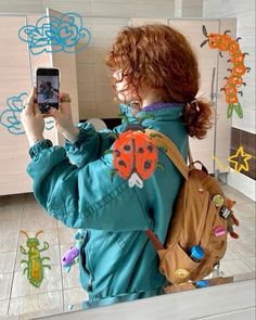 a woman taking a selfie with her cell phone in front of some drawings on the wall