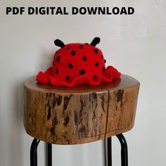 a crocheted ladybug hat sitting on top of a wooden table next to a white wall