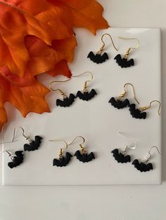 six pairs of black acrylic dangle earrings on a white plate next to an orange flower