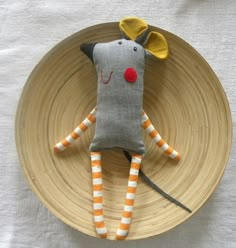 a stuffed animal is sitting on top of a wooden plate with orange and white striped legs