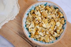 a bowl filled with cauliflower sitting on top of a wooden cutting board next to a white towel