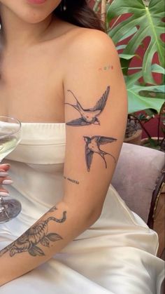 a woman with a hummingbird tattoo on her arm holding a glass of white wine