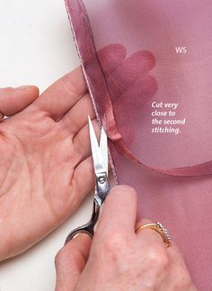 a person cutting fabric with scissors on top of a piece of pink organe ribbon