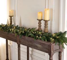 three candles are lit on a mantle with evergreen garland