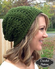 a woman wearing a green crochet hat in front of a fence and trees