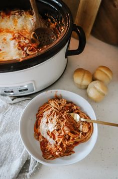 a white bowl filled with spaghetti and sauce next to some bread rolls on a table